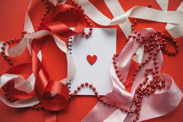 Festive background with ribbons and beads. In the middle is a notebook with a heart. — Stock Photo, Image