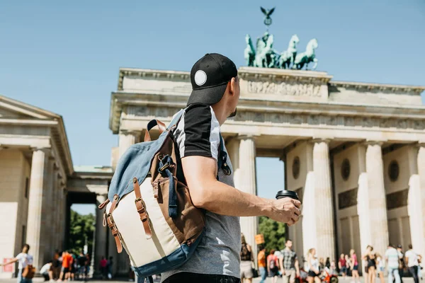 Una persona sostiene una taza desechable con café u otra bebida en el fondo de la Puerta de Brandeburgo en Berlín . — Foto de Stock