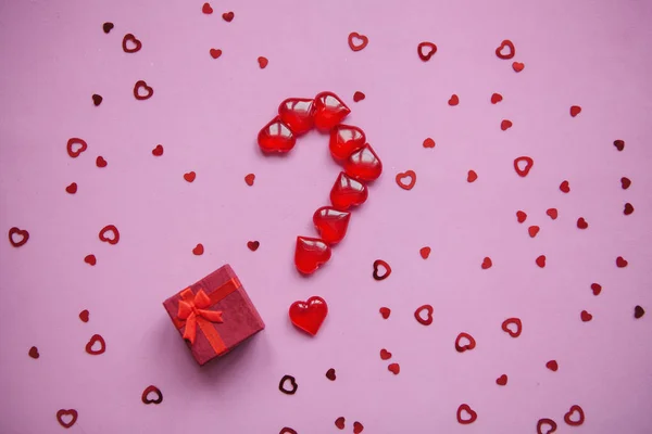 A box with a gift and a number of question marks laid out from small red hearts.