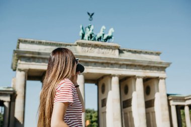 Bir kişi tek kullanımlık bir fincan kahve ya da Berlin Brandenburg Kapısı'nın arka planda başka bir içecek ile tutar.