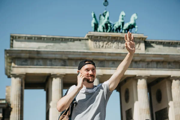 Egy turista vagy egy srác egy hátizsák mobiltelefonon beszél és köszönti valaki, a kezével. — Stock Fotó