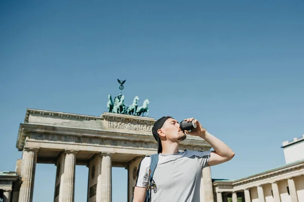 A person holds a disposable cup with coffee or another drink on the background of the Brandenburg Gate in Berlin. — Stock Photo, Image