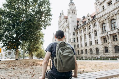 Genç bir adam Almanya'da Leipzig sokakta bir bankta oturuyor.