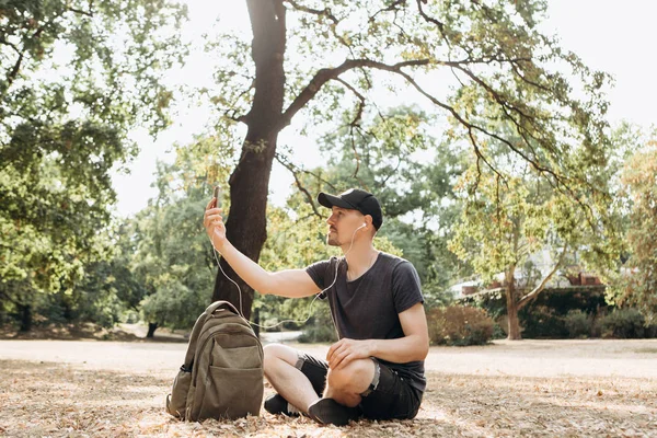 Egy fiatal srác, vagy diák, beszél a mobiltelefonján keresztül videó-kapcsolat vagy hallgató-hoz zene vagy néz egy video-ban egy őszi park — Stock Fotó
