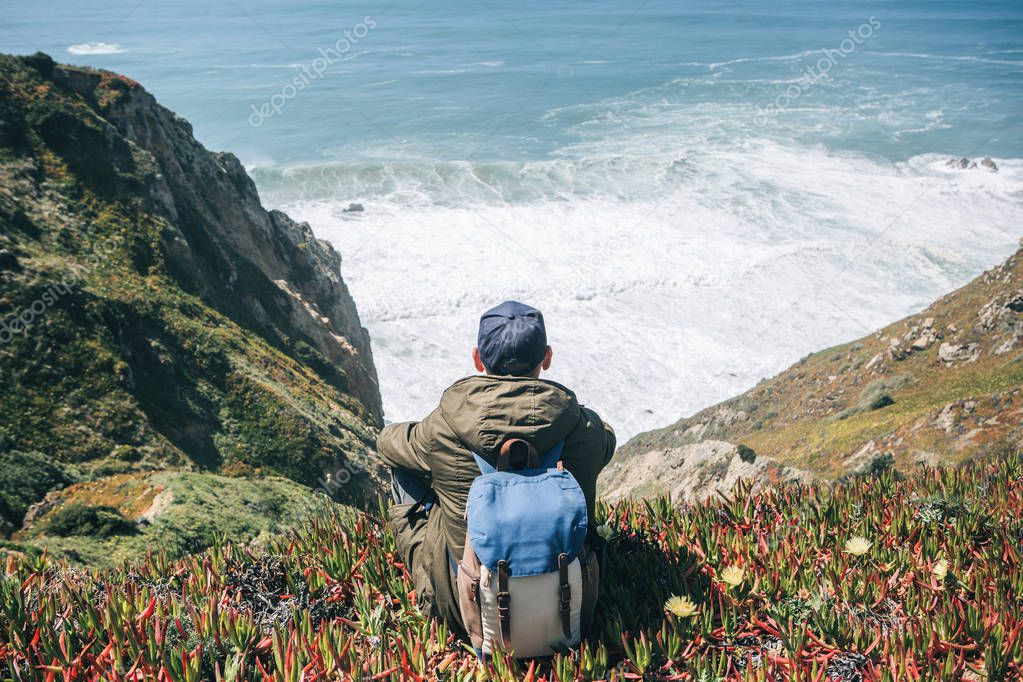 A tourist man with a backpack enjoys a beautiful view of the Atlantic Ocean on a spring day