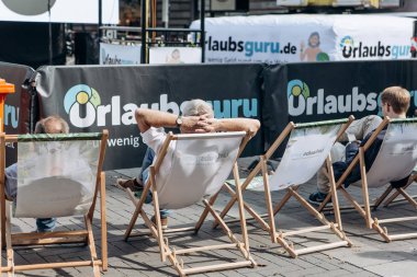 İnsanlar sandalyelerde oturup bir şehir caddesinde dinlenebilirler..