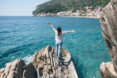 Bir kız kayalık bir sahilde duruyor.