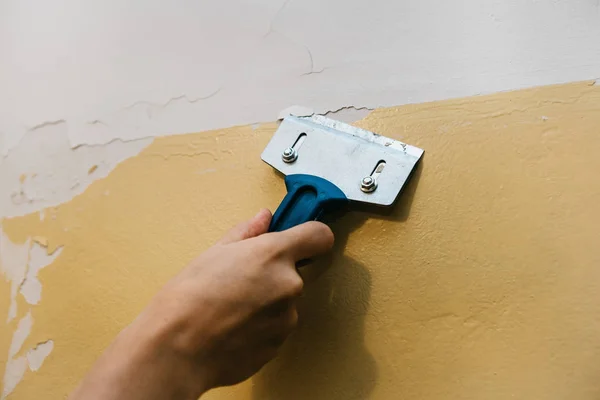 Ein Mann mit einem Schaber entfernt die alte Verkleidung von der Wand. — Stockfoto