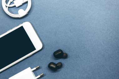 Mavi arka planda cep telefonu, kablosuz kulaklık ve şarj aleti..