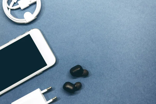 Mavi arka planda cep telefonu, kablosuz kulaklık ve şarj aleti..