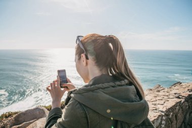 Bir turist cep telefonuyla güzel bir deniz manzarası çeker ya da hafızası için video kaydeder..