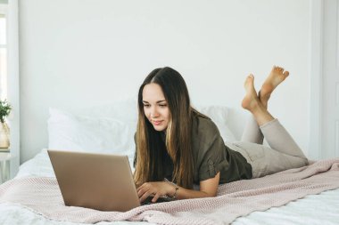 Pozitif kız öğrenci yatakta yatar ve dizüstü bilgisayar kullanır. İnternette mesajlaşıyor ya da sörf yapıyor..