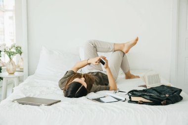 Kız öğrenci ya da kız öğrenci yatağında yatıyor ve dersten sonra evde cep telefonu kullanıyor..