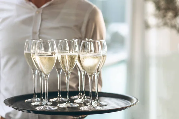 The waiter is holding a tray with glasses of champagne or white sparkling wine. Service in the restaurant.