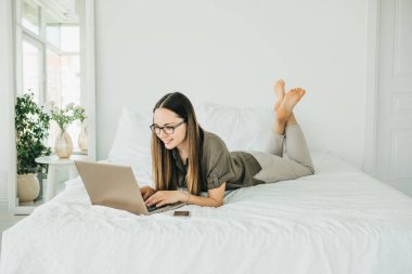 Pozitif kız öğrenci yatakta yatar ve dizüstü bilgisayar kullanır. İnternette mesajlaşıyor ya da sörf yapıyor..