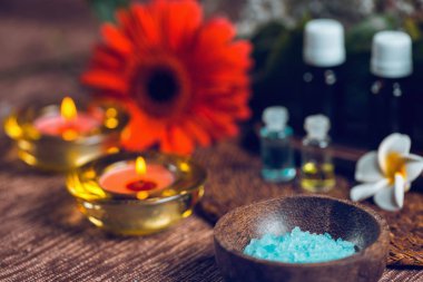 Aromaterapi kompozisyon ile deniz tuzu ahşap kase, mavi ve yeşil temel yağlar, kırmızı ve turuncu renkli çiçekler ve kırmızı mum dolu saydam aromaterapi şişe. Aromaterapi rahatlamak kavramı.