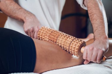 Anti-Selülit selülit Madero terapi el masaj ahşap oklava ile güzel genç sportif kadın beyaz havlu üzerinde tedavi sırasında yalan yakın çekim