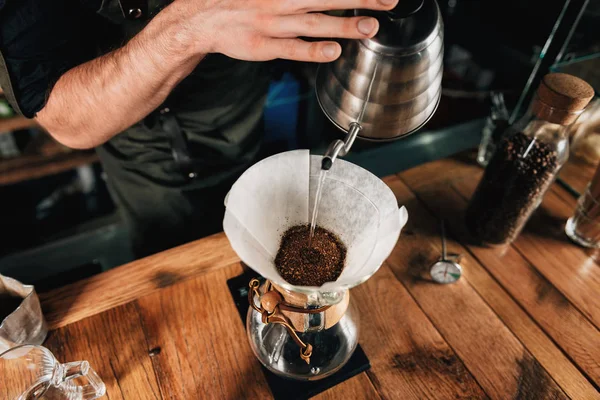 Beyaz filtre filtre kahve için içine su ısıtıcısı kaynar su dökülen Barista. Karanlık üniforma, ahşap tablo.    