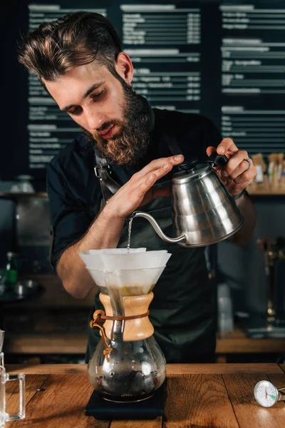 年轻的男性咖啡师将开水从水壶里倒出来过滤咖啡 穿着深色制服的巴里斯塔 — 图库照片