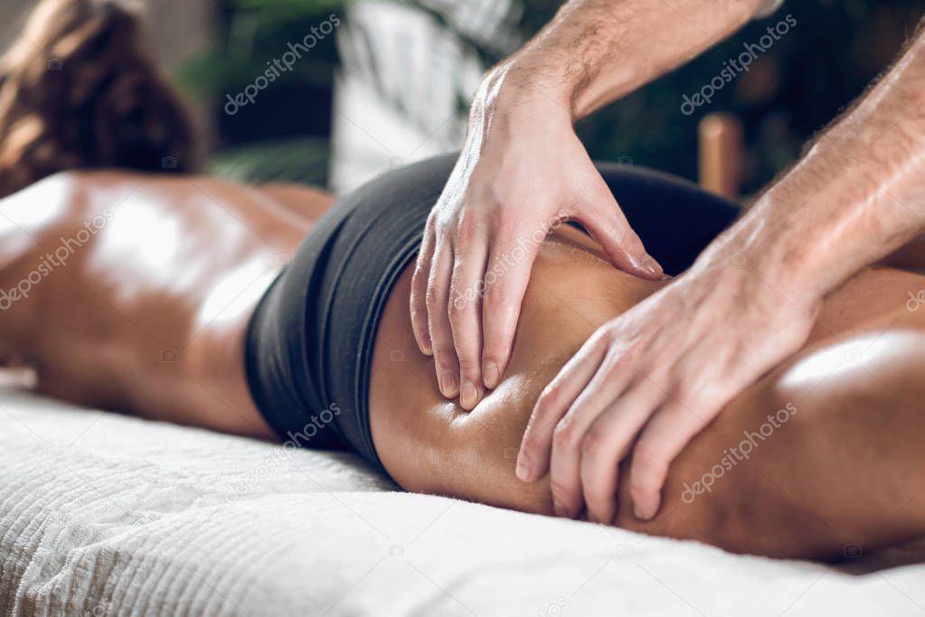 Close up of therapist doing anti cellulite Madero therapy hand massage to attractive sporty young woman, lying on white towel