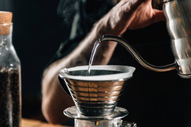 Bir genç erkek barista dökme kaynar su içine Kalita dalga Kahve demlemek ve kafede dijital ölçek ölçmek için damlatıcı kapatın. Barista karanlık üniforma giydiği bildirildi. Damla Brew Kahve masada yapmak için donatım.