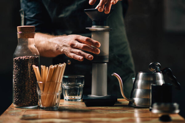 Горизонтальное изображение баристы, делающей кофе с воздушным прессом. Бариста с татуированными руками в тёмной форме
. 