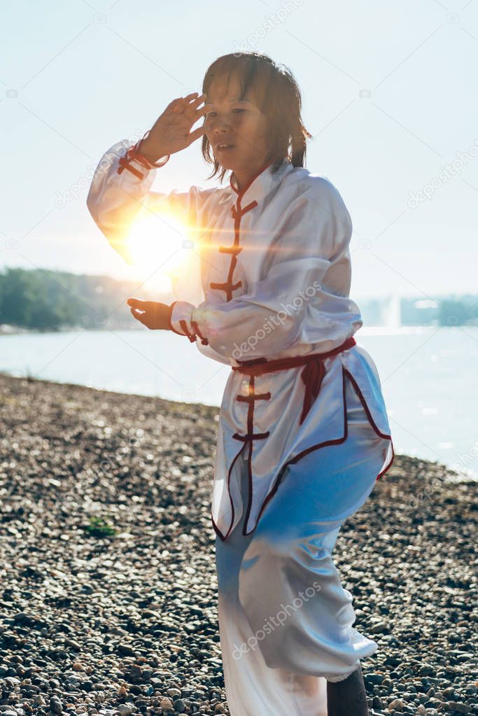 Asian Woman in traditional clothing practicing Tai Chi by the lake