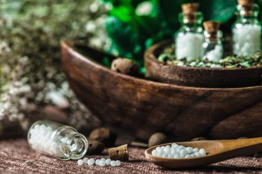 Tahta kaşık Homeopatik globülleri, arka planda homeopatik ilaç andfresh yapraklarla küçük şişe dolu