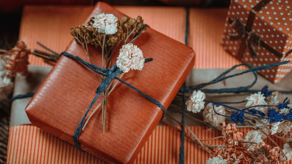 Horizontal composition with gift boxes wrapped in natural terracotta color paper, tied with twine, decorated with dried flowers.