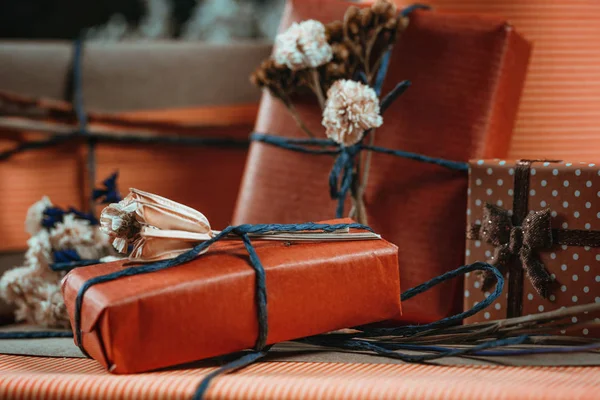 Horizontal composition with gift boxes wrapped in natural terracotta color paper, tied with twine, decorated with dried flowers.