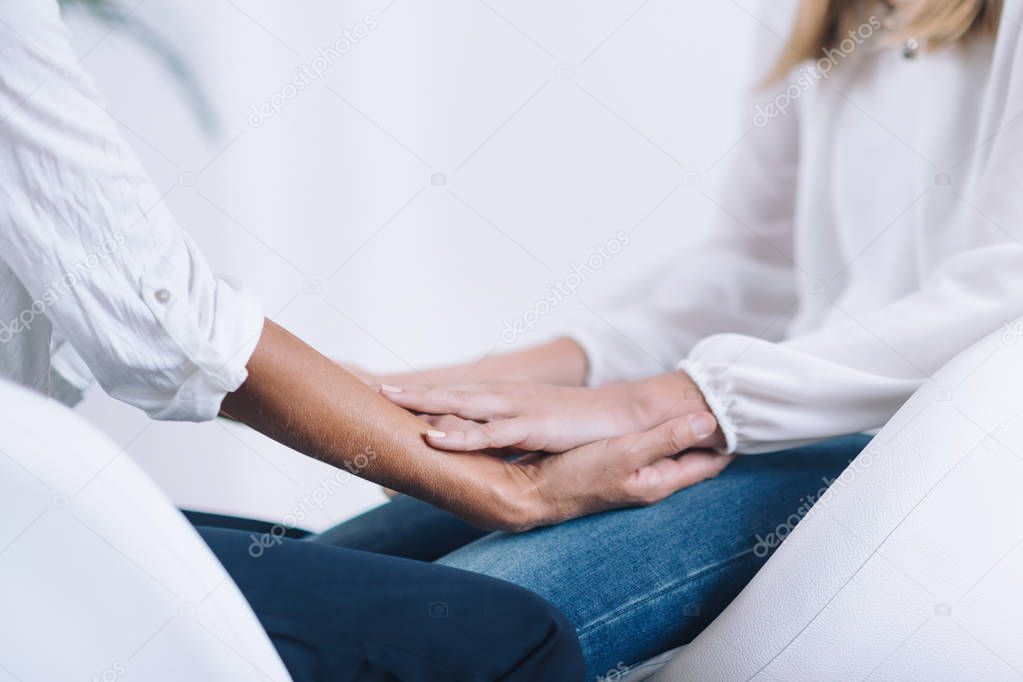 Female Theta healing therapist performing alternative therapy treatment with young woman patient. Therapist holding hands and transfer energy. Wearing white clothes.