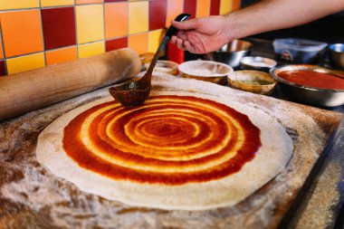 Şef pizza hamur pizza restoranında metal bir kepçe ile domates sosu yayılıyor. Pizza yapma süreci.