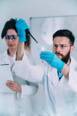 Damlalık ve Test tüpü tutan, beyaz önlük giyen genç erkek araştırmacı