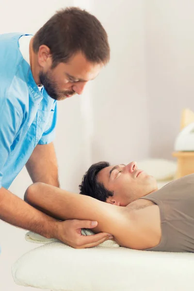 物理治疗师在人的手臂上做治疗 治疗师穿蓝色制服 脊椎按摩调整 病人躺在按摩床上 — 图库照片