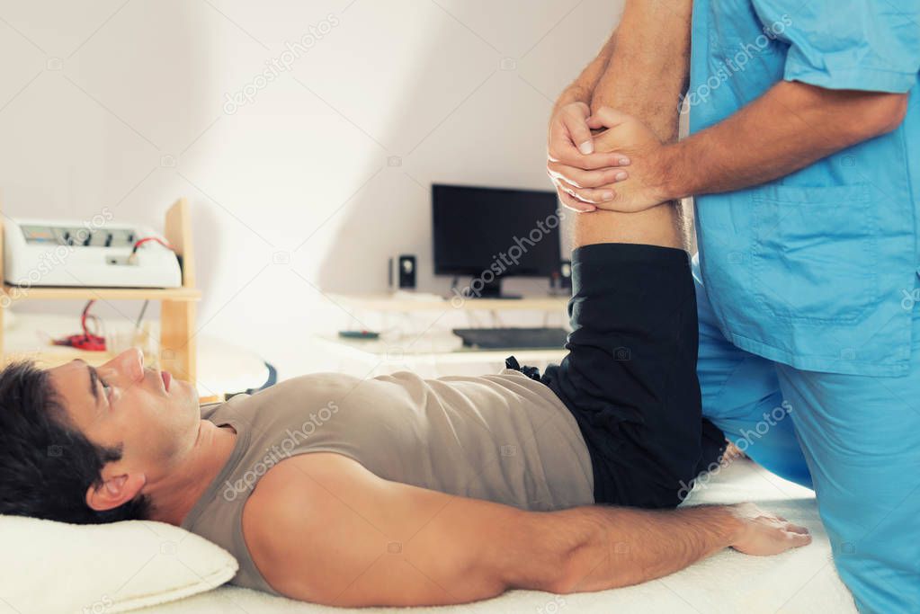 Physiotherapist doing healing treatment on patient leg. Therapist wearing blue uniform. Osteopathy. Chiropractic adjustment, patient lying on massage table