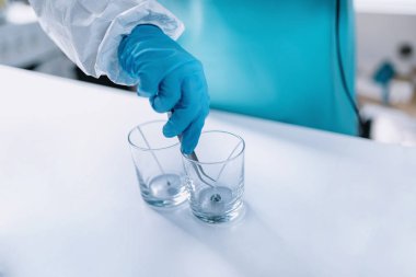 İki bardak altındaki pamuk fitil yapıştırma kadın mum yapımcısı. İşlem yapma mum. Koruyucu iş giysisi giymiş.