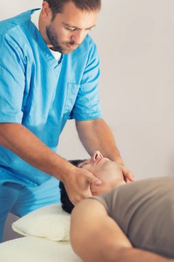 Adamın boynundaki iyileştirici tedavi yaparken mavi üniforma giyen terapist, kırıkçı, Chiropractic ayarlama, Masaj masanın üzerinde yatan hasta fizyoterapist