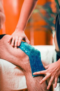 Mavi buz torbası ağrılı diz üstünde tutarak.