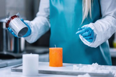 Maker giyiyor mavi koruyucu iş giysisi ve turuncu mum kalıp üzerinden yaptırmayı mum. Mum yapma süreci  