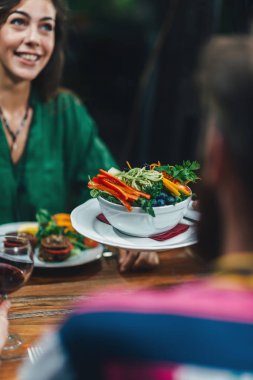 Restoranda lezzetli vejetaryen karışık organik salata tabağı çift gülümseyen genç garson garsona dikey görüntü.
