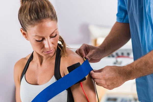 Electrical stimulation in physical therapy. Therapist positioning electrodes on a patient's shoulder