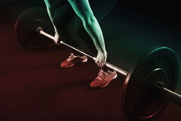 Filtered image of female prepares to lift heavy barbells at the gym.