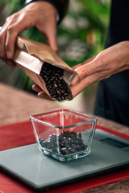 Kahve tanelerini dijital ölçekte tartmak. Kadın barista elleri kahve demlemeden önce bir ölçekte kavrulmuş kahve taneleri dökme. 