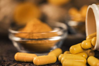 Curcumin ek kapsüller, cam kase zerdeçal tozu ve arka planda curcuma kökü. İltihapkarşı Bitkisel ilaç Curcuma