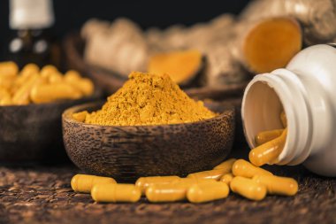 Curcumin ek kapsüller, cam kase zerdeçal tozu ve arka planda curcuma kökü. İltihapkarşı Bitkisel ilaç Curcuma