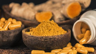 Curcumin ek kapsüller, cam kase zerdeçal tozu ve arka planda curcuma kökü. İltihapkarşı Bitkisel ilaç Curcuma