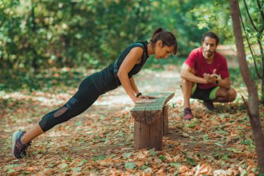 Parkta kişisel antrenörüyle şınav çeken bir kadın.