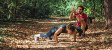 Parkta kişisel antrenörüyle şınav çeken bir kadın.