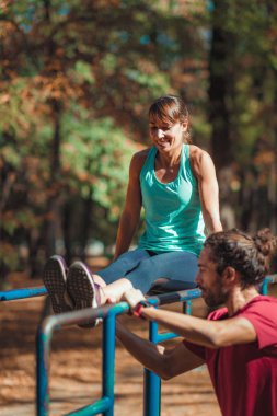Parktaki paralel barda antrenörle egzersiz yapan bir kadın.