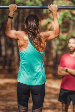 Parkta kişisel antrenörüyle barfiks çeken bir kadın.
